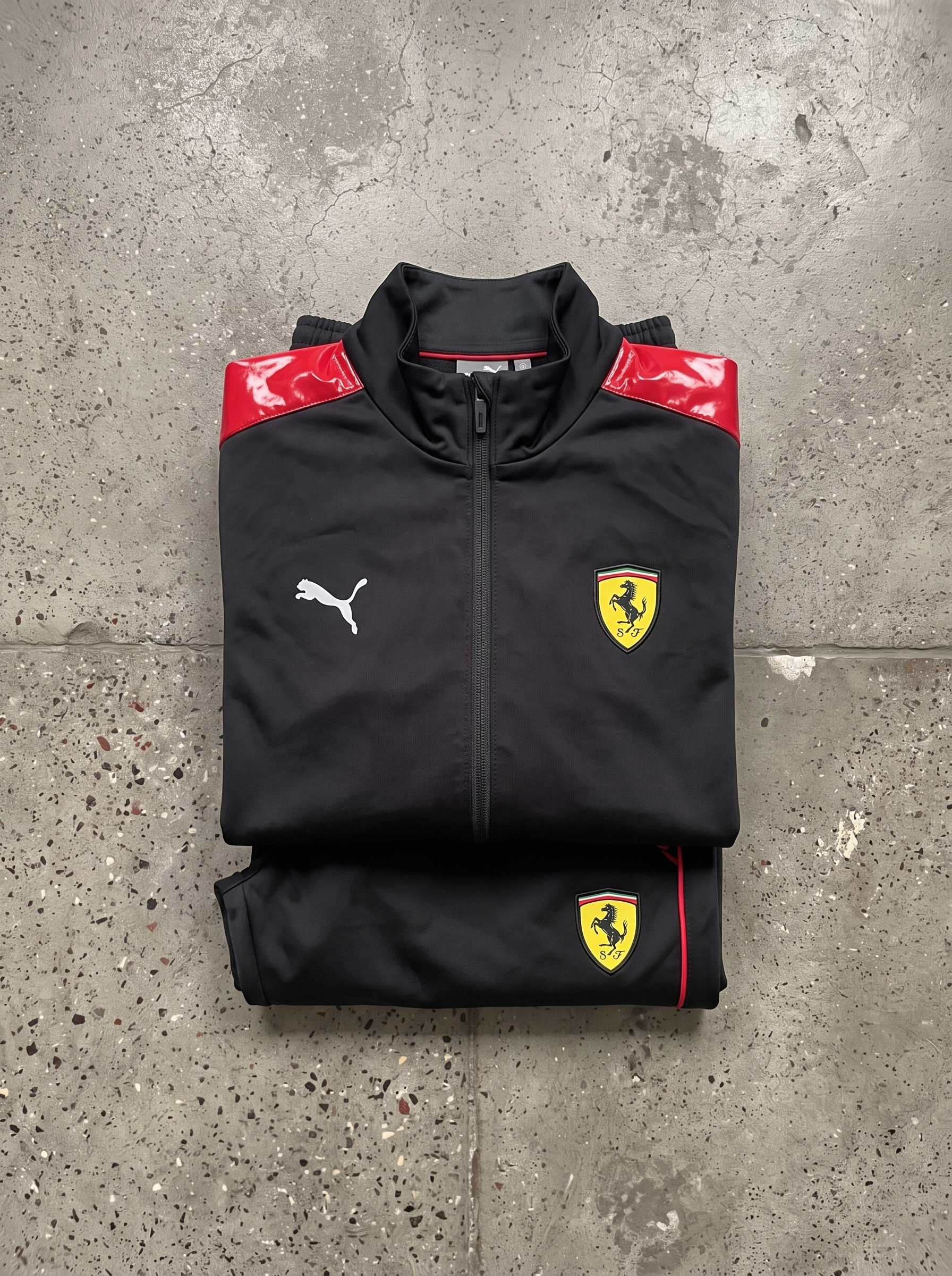 Zusammengelegter schwarzer Ferrari-Trainingsanzug mit roten Details auf Steinboden