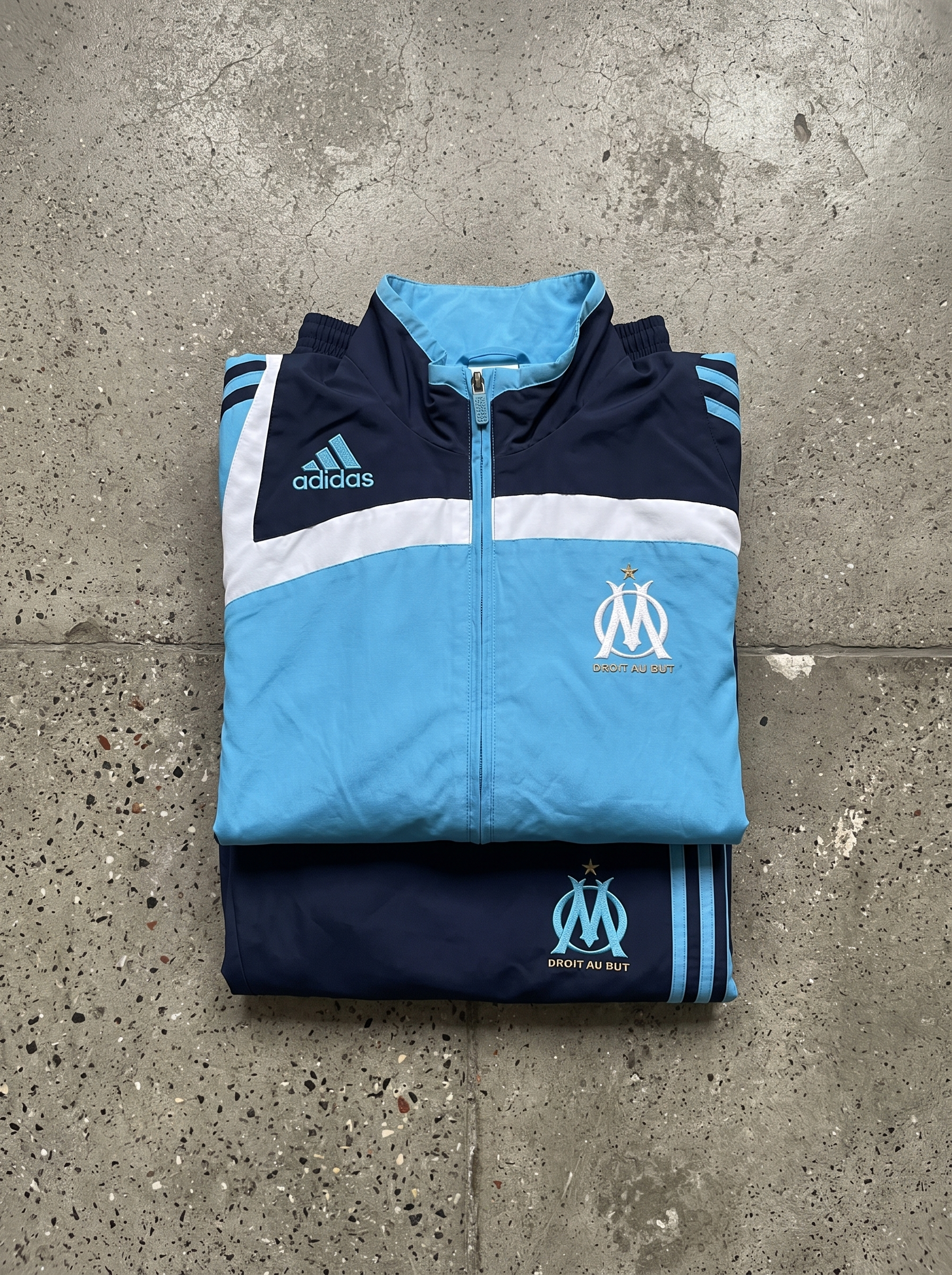 Zusammengelegter hellblau-dunkelblauer Olympique-Marseille-Trainingsanzug auf Steinboden